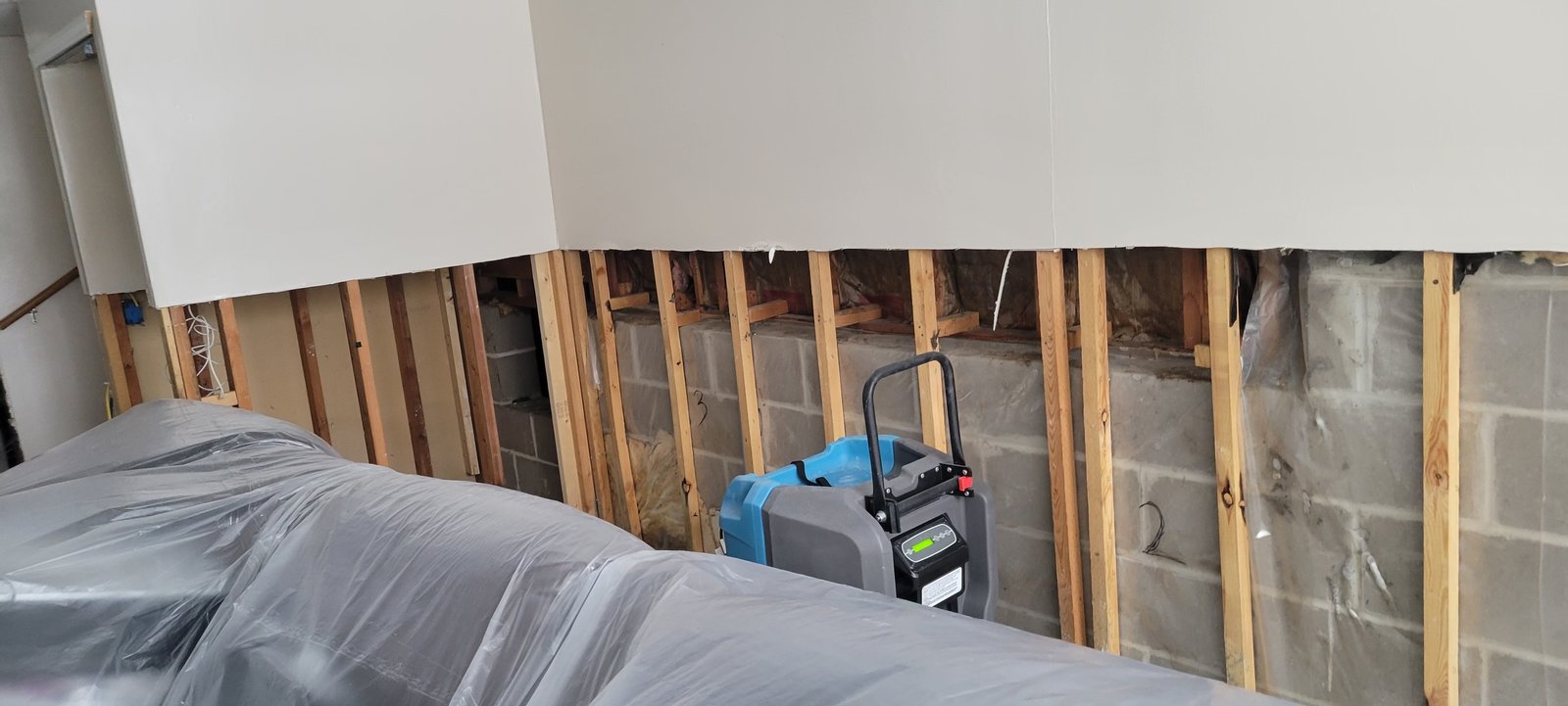 Flood cut in a finished basement with wall insulation exposed and a dehumidifier running during structural drying