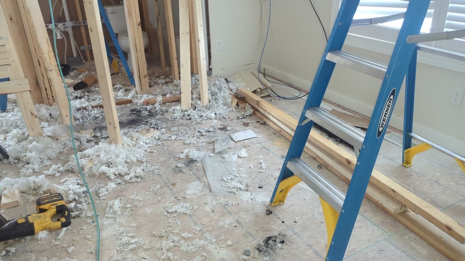 Interior walls stripped to the studs with wet insulation pulled onto the subfloor during a water damage tear-out